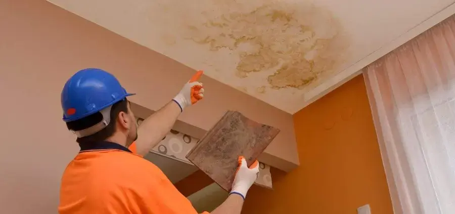 Worker in a hard hat inspecting a water-stained ceiling panel