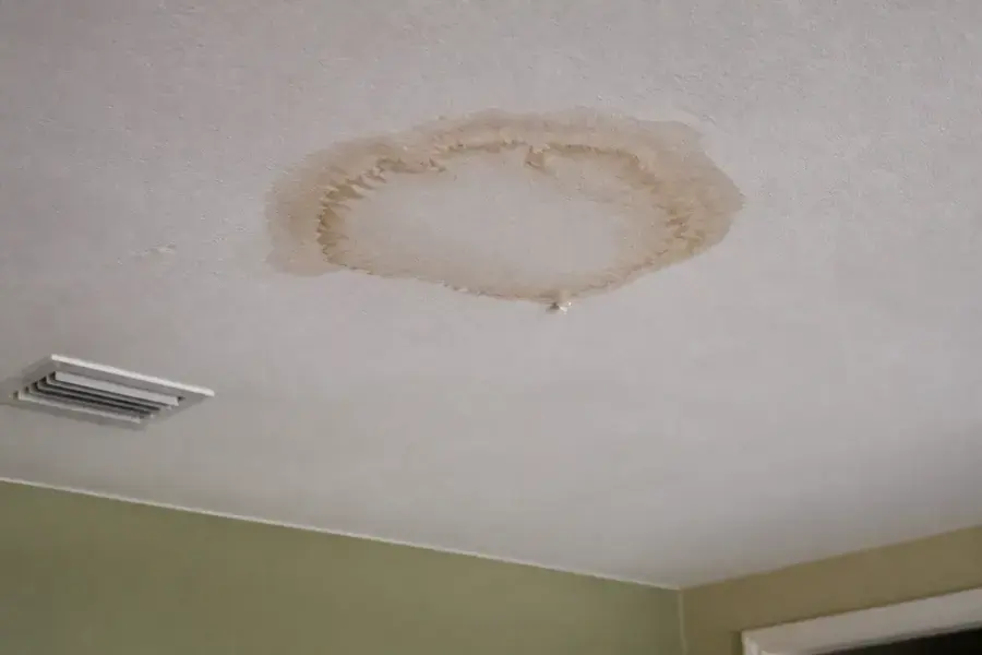Round brown water stain on a ceiling above a supply vent