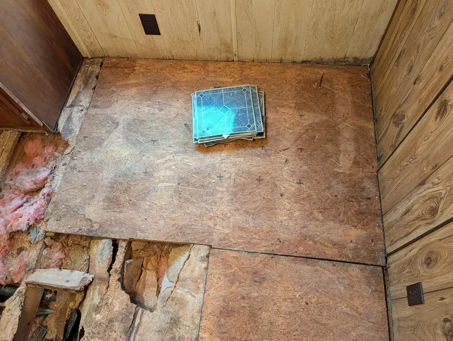 Room with damaged subfloor sections cut open to the insulation