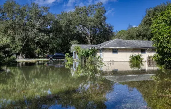 Single-story home surrounded by standing floodwater under tall trees