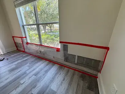 Room with a flood cut along the bottom of the wall marked in red tape above a plank floor