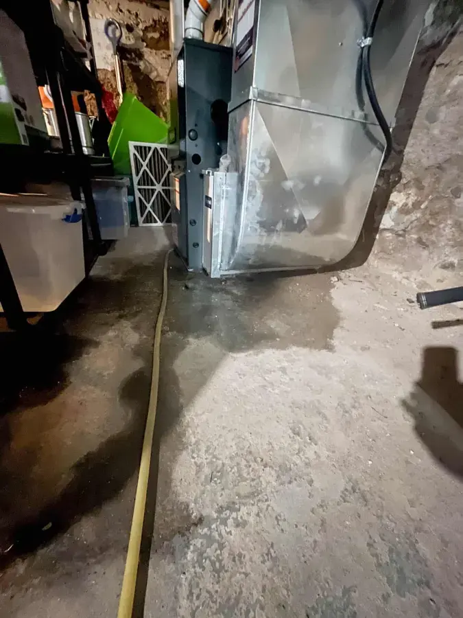 Air handler in a garage with water spread across the concrete floor beneath it