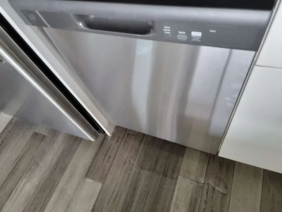 Water spreading across vinyl plank flooring at the base of a stainless dishwasher