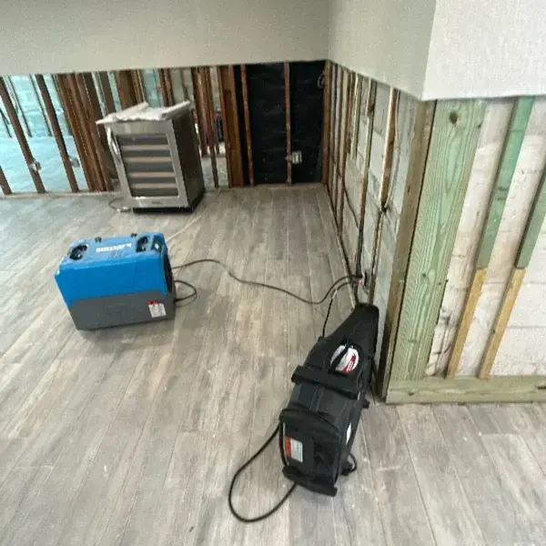 Dehumidifier and air mover drying a room with the lower walls opened to the studs